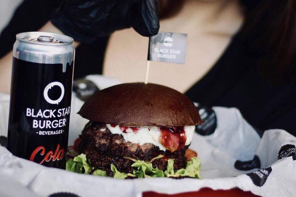 A Black Star Burger on a black bun, served beside the brand's own cola can.